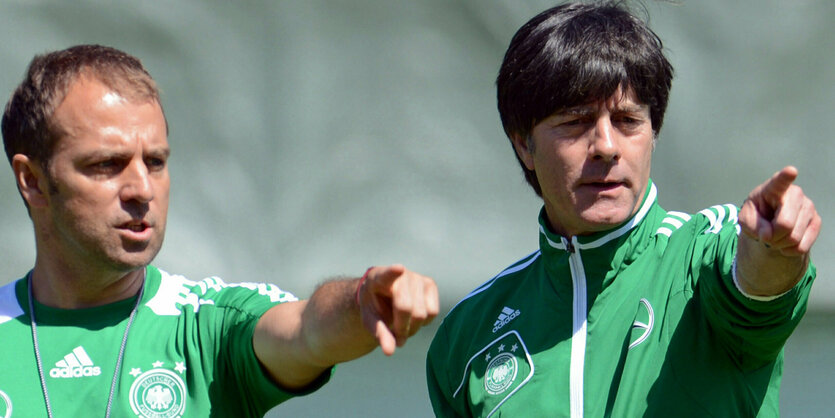 Flick und Löw zeigen mit ausgestrecktem Fingere und Arm am Spielfeldrand in die gleiche Richtung