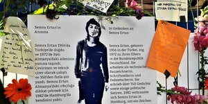 An einem Zaun in St. Pauli hängt ein Plakat zur Erinnerung an Semra Ertan, Blumen sind um es herum befestigt und Zettel mit Gedichten.