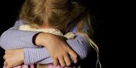 Ein kleines Mädchen sitzt zusammengekauert hinter ihrem Kuscheltier versteckt und weint