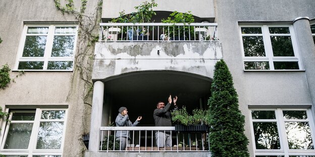 Menschen applaudieren auf Altbau-Balkon