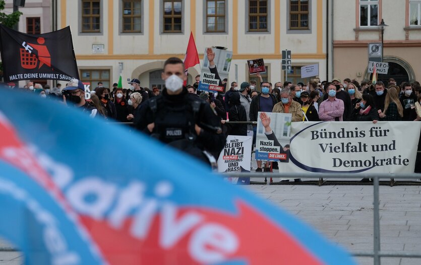 Eine AfD-Flagge im Vordergrund, im Hintergrund linke Protestierende