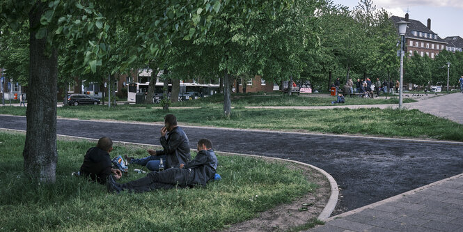 Drei Männer ruhen sich unter einem Baum an einer Straßenecke aus