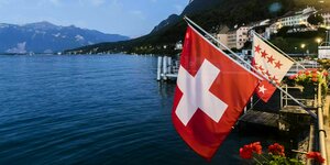 Eine Schweizer Fahne an einem flattert am Ufer eines Sees