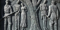 Das Denkmal zeigt Zwei Soldaten in Uniform und mit Gewehren. Sie stehen vor einem Baum an dem drei Menschen aufgehängt sind.