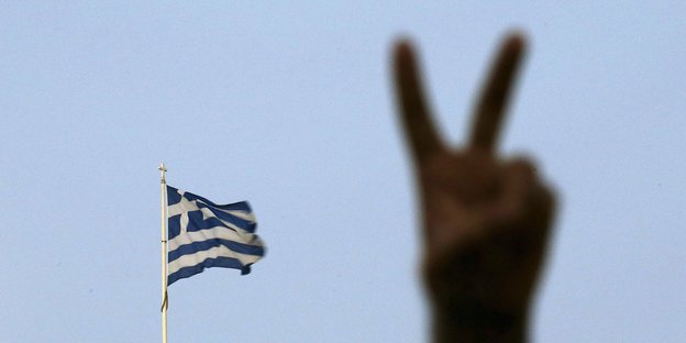 Eine Hand macht das Victory-Zeichen, im Hintergrund die griechische Fahne