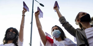 Drei junge Frauen halten Papierflieger in die Luft. Sie tragen teilweise belarussische Widerstandsfahnen.