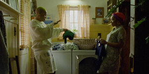 Szene aus der Serie: Das Paar steht vor der Waschmaschine, tanzt und legt Wäsche zusammen