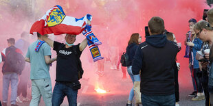 Ein mann tanzt mit einer bleu-weiß-roten Fahne, dahinter brennt ein begalisches Feuer