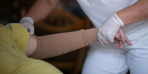 Eine Pflegerin zieht während ihrer Schicht in der ambulanten Pflege einem Klienten einen Kompressionsärmel an.