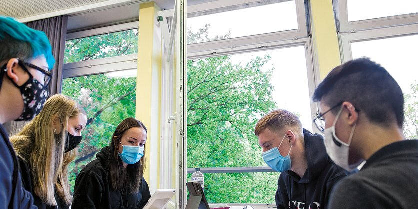 Schüler und Schülerinnen sitzen mit Maske um einen Tisch.