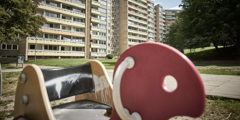 Ein mit Farbe beschmiertes Wipptier für Kinder steht auf einen Spielplatz vor einem Hochhausblock.