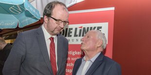 Ein sehr großer Mann spricht zu einem kleinen Mann vor rotem "Die Linke"-Hintergrund