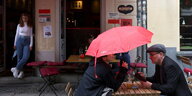 Zwei Besucher sitzen im Außenbereich eines Restaurants mit einem Regenschirm