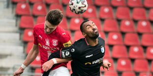 Zwei Fußballspieler springen in die Luft und wollen einen Ball köpfen.