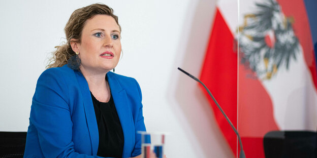 Susanne Raab während einer Pressekonferenz neben der österreichischen Flagge