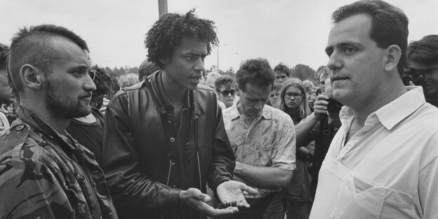 Ein Demonstrant diskutiert mit Anwohnern vor dem ausgebrannten Wohnheim für Asylbewerber:innen, Rostock Lichtenhagen, 1992.