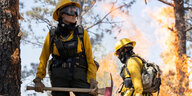 Eine Feuerwehrfrau steht in voller Montur in einem brennenden Wald