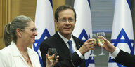 Izchak Herzog stößt mit seiner Frau und einer weiteren Person an - im Hintergrund Israel - Flaggen