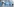 Eine Gruppe von Personen in blauen Schutzanzügen wird von einer Person in einem weißen Schutzanzug mit Desinfektionsmittel besprüht