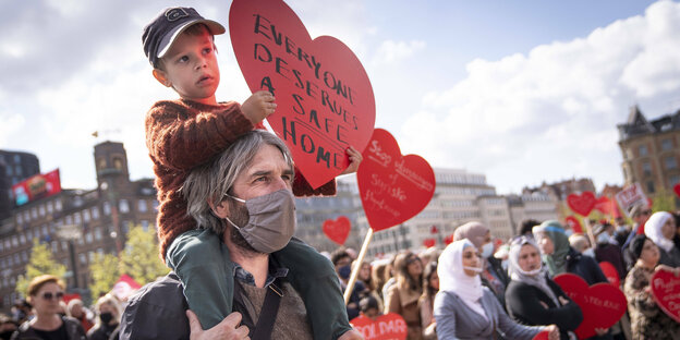 Demonstranten mit herzförmigen Schildern mit Aufschriften - ein Junge sitzt auf den Schultern seines Vaters und hält ein Schild mit der Aufschrift "Everybody deserves a home"