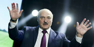 Alexander Lukaschenko gestikuliert mit erhobeben Händen im Scheinwerferlicht