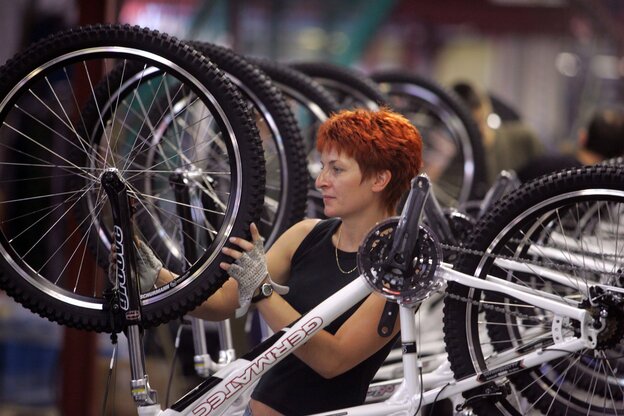 Eine Frau schraubt an einem Fahrrad in einer Produktionsstraße mit lauter weiteren Rädern hinter ihr. Eine Frau schraubt an einem Fahrrad in einer Produktionsstraße mit lauter weiteren Rädern hinter ihr.