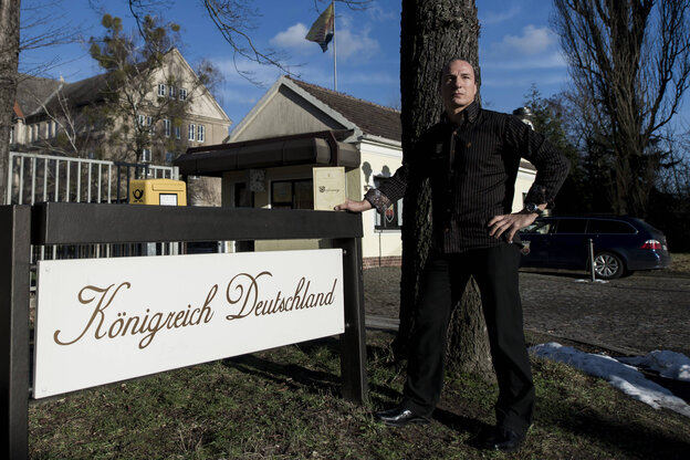 Ein Mann steht neben einem Schild mit der Aufschrift "Königreich Deutschland" Ein Mann steht neben einem Schild mit der Aufschrift "Königreich Deutschland"