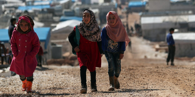 Drei Mädchen laufen einen Weg in einem Flüchtlingslager hinauf - sie tragen Kopftücher