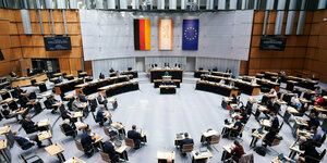 Das Bild zeigt den Plenarsaal, des Abgeordnetenhauses, fotografiert von der Pressetribüne mkt Blick auf drei Flaggen an der gegenüber liegenden Wand: die Berliner, die deutsche und die der Europäischen Union.