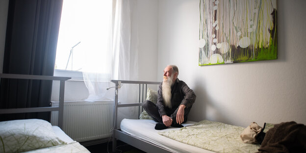 Ein Mann mit weißem Bart sitzt auf einem Bett