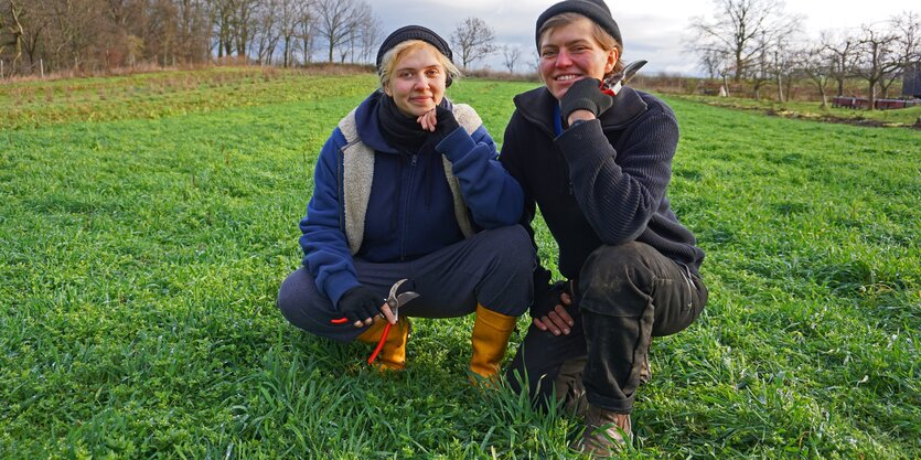 Zwei Frauen knien auf einem grünen Acker