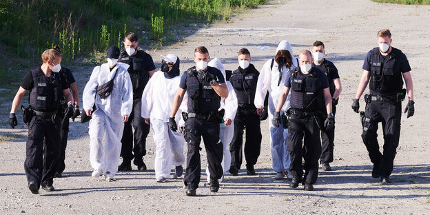 Eine Reihe von Polizisten gleiten Umweltaktivistinnen in weißen Schutzanzügen