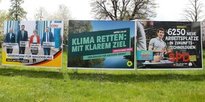Drei Wahlplakate stehen auf einer Wiese