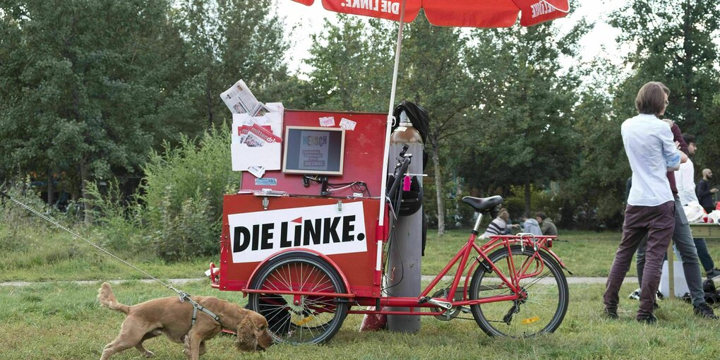 Ein Lastenfahrrad, das zu einem kleinen Wahlkampfstand der Partei die Linke umgebaut wurde. Ein Hund läuft vorbei