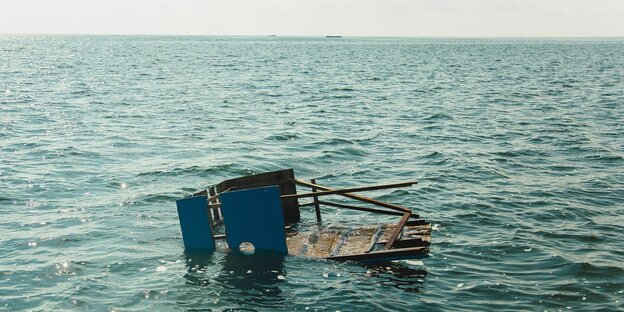 Zerstörtes Boot trebt bei Sonnenschein in türkis blauen Wasser