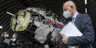 ein Mann mit Maske vor einem Flugzeugwrack