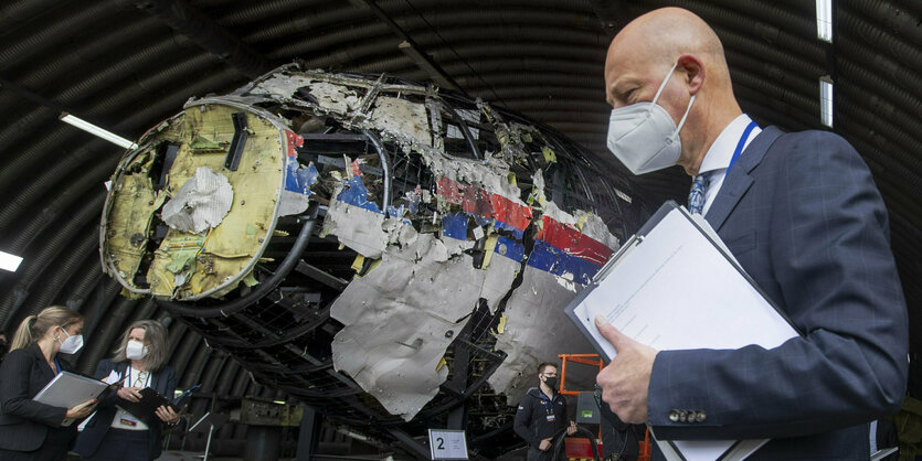 ein Mann mit Maske vor einem Flugzeugwrack