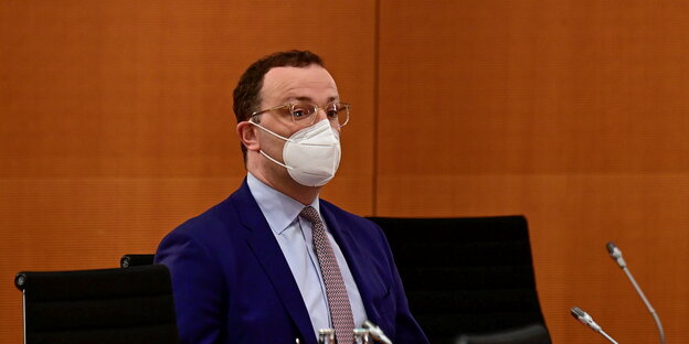 Jens Spahn sitzt mit Maske hinter einem Pult mit Mikrofon