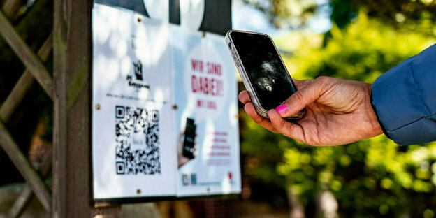 Eine Frau fotografiert mit ihrem Smartphone einen QR-Code an dem Tor eines Restaurants ab