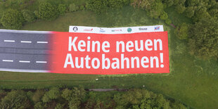 Blick von oben auf riesiges Transparent, das 2 Fahrspuren zeigt, die in eine rote Fläche übergehen mit der Aufschrift: "Keine neuen Autobahnen",