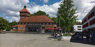 Ein gepflasterer Platz mit Menschen auf Bänken vor rotem Gebäude