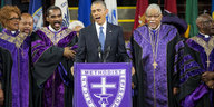 Barack Obama am Rednerpult in einer Kirche, hinter ihm Geistliche