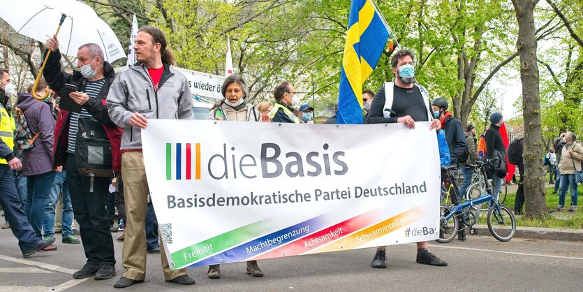 AnhängerInnen der Partei „die Basis“ tragen ein Banner mit dem Logo der Prtei die Basis während einer Domonstration