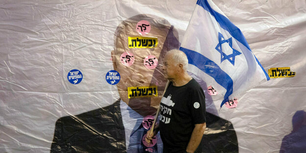 Ein israelischer Demonstrant hält während einer Demonstration vor der Residenz des Premierminister eine Fahne, während er an einem Banner vorbeiläuft, das den israelischen Premierminister Benjamin Netanjahu zeigt. Auf Hebräisch ist zu lesen: "Sie haben v