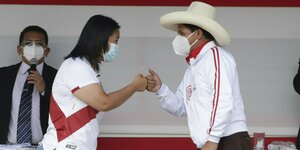 Frau Fujimori (lange schware Haare) und Herr Castillo (Cowboyhut) tragen jjeweils eine Maske und drücken zur Begrüßung Fäuse aneinander.