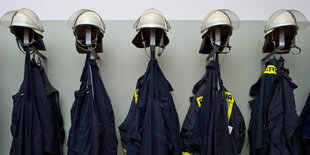 Mehrere Feuerwehrjacken und -helme hängen an einer Garderobe.