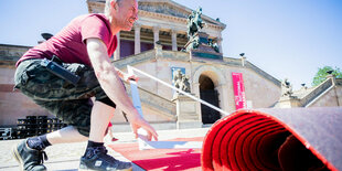 Mann verlegt vor der Alten Nationalgalerie Roten Teppich für die Berlinale