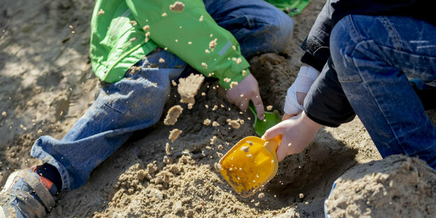 Zwei Kinder spielen mit Schaufel im Sandkasten