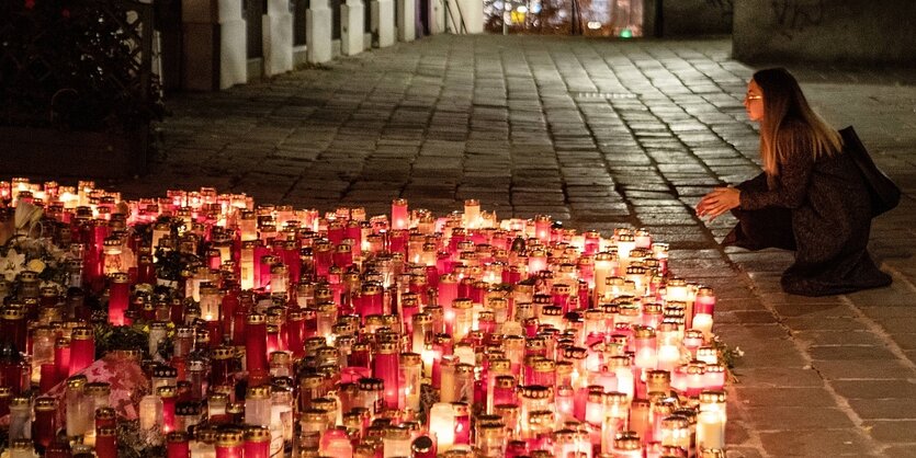 eine Frau kniet neben einem Meer von Friedhofskerzen