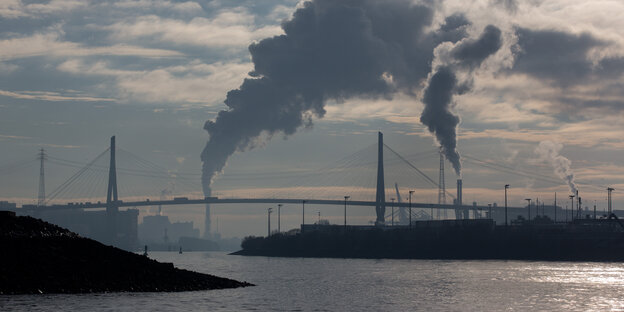 Die Köhlbrandbrücke vor den rauchenden Schloten von Industrieanlagen.
